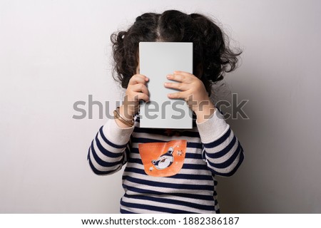 Little girl holding a children story book with blank cover in front of her face, editable template ready for your design, cover selection path included.