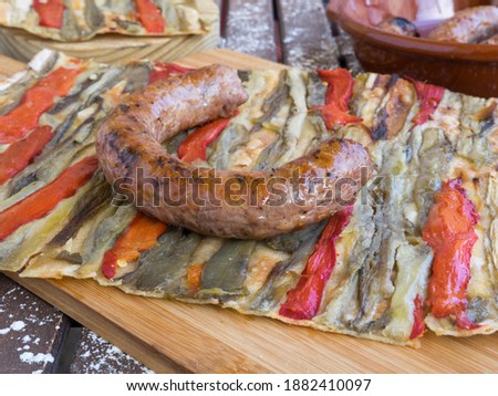 a slice of coca de recapte, a typical Catalan pizza-like savory pie, made with grilled aubergines and red pepper, and pork sausage, on a rustic wooden table.Spanish cuisine concept