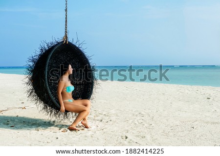 Happy female traveller in turquoise swimsuit  is enjoying her summer vacation on a swing coconut at a tropical beach with white sand