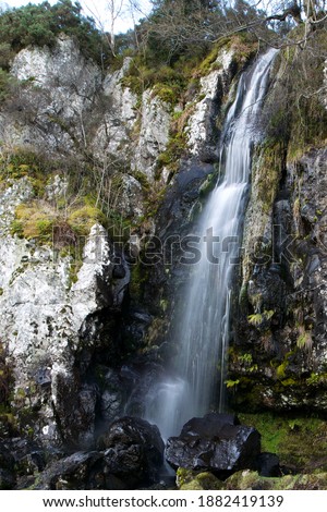 High thin waterfall in frozen Gargunnock Hills in Scotland falling on a big rock