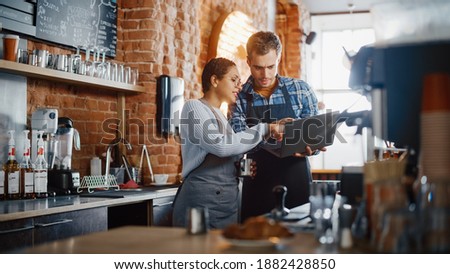Two Diverse Entrepreneurs Have a Team Meeting in Their Stylish Coffee Shop. Barista and Cafe Owner Discuss Work Schedule and Menu on Laptop Computer. Multiethnic Female and Male Restaurant Employees. Royalty-Free Stock Photo #1882428850