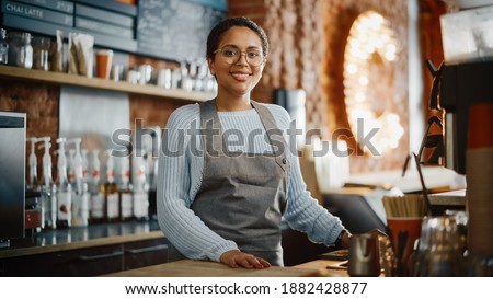 Beautiful Latin American Female Barista with Short Hair and Glasses is Projecting a Happy Smile in Coffee Shop Bar. Portrait of Happy Employee Behind Cozy Loft-Style Cafe Counter in Restaurant. Royalty-Free Stock Photo #1882428877