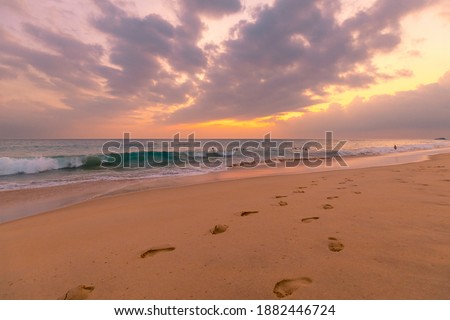 Beautiful ocean sandy beach under sunset sky with footprints in a sand.