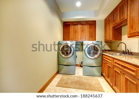 Rectangle laundry room with wooden cabinets and modern shiny appliances