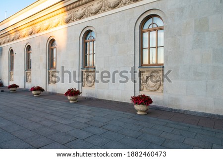 One story building of large blocks of yellow limestone with arched windows and vases of flowers in front of the facade, sunny