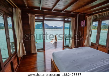Travel Woman in White Dress Sitting Outdoor near Wooden House on Water. View on Tourist Woman Relaxing and Leisure from Raft House on Cheow Lan Lake in Thailand. Eco Tourism Royalty-Free Stock Photo #1882478887