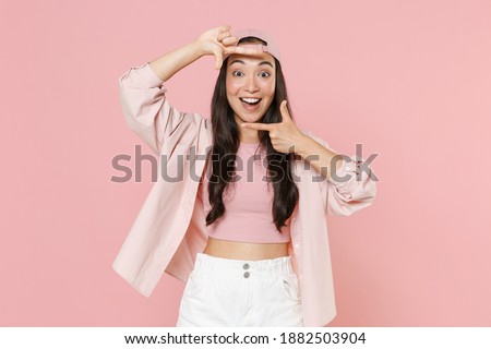 Excited young asian woman 20s in casual clothes cap posing isolated on pastel pink wall background studio portrait. People lifestyle concept. Mock up copy space. Making hands photo shot frame gesture