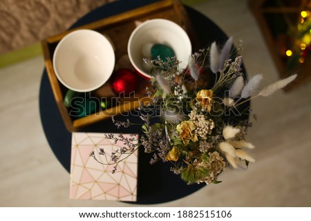 Cup and glass with print snowman on wooden table, shimmering lights. dried flowers on a wooden tray with a gift box for christmas or new year decoration bouquet composition