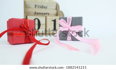 Wooden calendar with dates. Next to it is a cardboard box with a bow. Isolated on a white background. Place for your text. January 01st on the calendar.