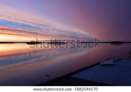 Beautiful landscape with pink sunrise over the lake this winter morning. Clouds and sky color reflections in the calm water next to the dock. Photo taken in Västerås, Sweden.