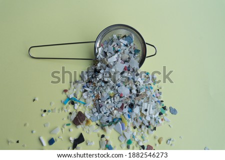 Stock photo of microplastics and kitchen strainer on a soft yellow background.
