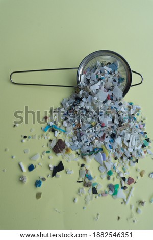 Vertical Stock Photo of Microplastics and Kitchen Strainer on Soft Yellow Background.