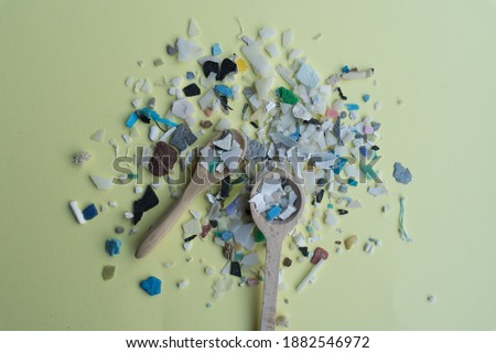 Stock photo of microplastics and two small wooden spoons on a soft yellow background.