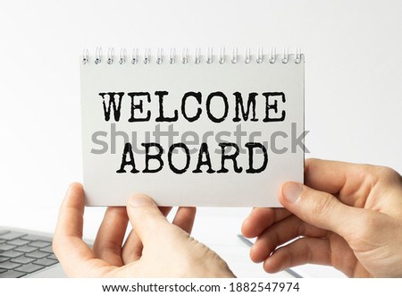 Businesswoman hands holding white card sign with welcome aboard text message isolated on grey wall office background. Retro instagram style image