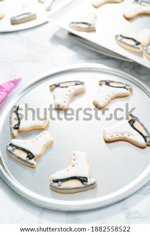 Decorating sugar cookies shaped as figure skates with royal icing.