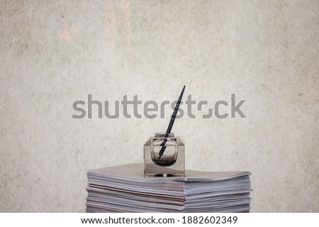 Inkwell with a dip pen and a penholder standing on a pile of paper. Such writing instruments were used before the emergence of pencils and fountain pens.

 Royalty-Free Stock Photo #1882602349