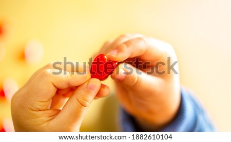 Little child holding a little red heart, close-up isolated on yellow beige gradation and copy space.