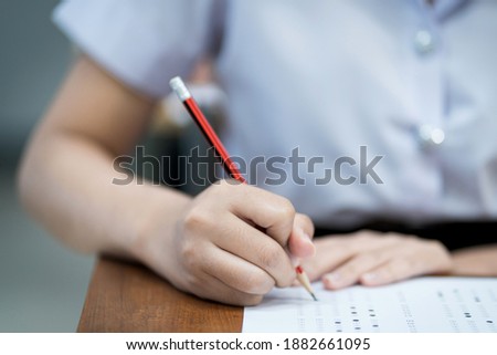 Close up of young university students concentrate on doing examination in classroom. Girl student writes on the examinations answer paper in the classroom.