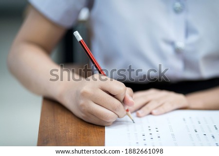 Close up of young university students concentrate on doing examination in classroom. Girl student writes on the examinations answer paper in the classroom.