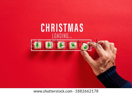 Male hand putting wooden cubes with tree icons in Christmas loading bar on red background. Christmas countdown or celebration concept.