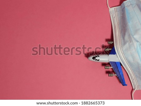 Toy airplane and medical mask on light pink background, flat lay with space for text. Travelling during coronavirus pandemic. Selective focus