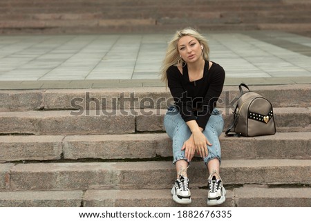 Teenager girl in jeans sitting outdoors on long stone stairs, cityscape.