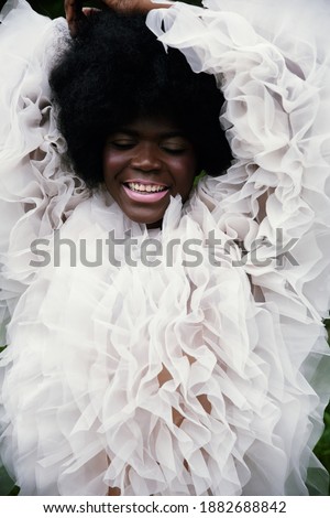 Alien. African beautiful model with perfect body in white tulle ruffles. Muscles, chocolate skin. Cold colors. Surreal exterior. Good emotions. Laugh and happiness
