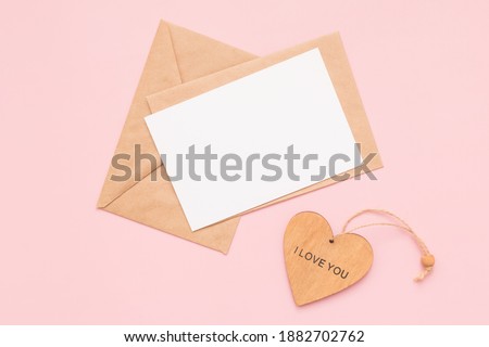 Craft envelopes, blank paper white card and wooden heart with the words I love you on a pink background. Place for text. Flat lay. Top view. Happy Valentines Day.