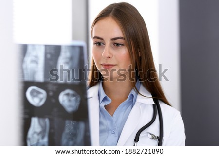 Doctor woman examining x-ray picture while standing near window in hospital. Surgeon or orthopedist at work. Medicine and healthcare concept