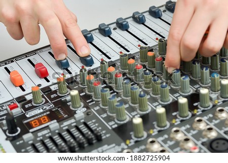 The boy moves the faders and potentiometers on the mixing console in a tilted view.