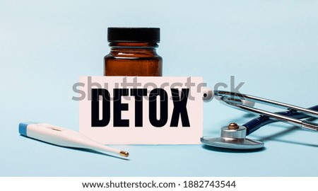 On a blue background - a bottle for pills, a stethoscope, an electronic thermometer and a card with the inscription DETOX. Medical concept