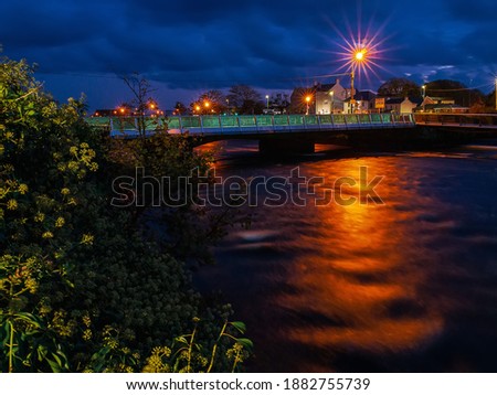 Night shot of Wolfe Tone Bridge in Galway city, Ireland, Blue sky, warm orange lights reflects in river Corrib. Pronounced lens star-burst.