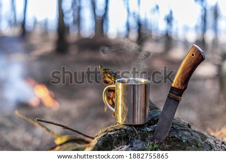 Tourist things - stainless camping cup of tea and special knife. Nature background.