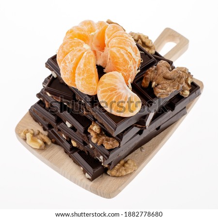 Peeled tangerine with walnuts on the pyramid of the pieces of the dark chocolate. Closeup image