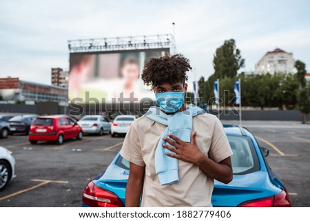 Portrait of young african american man in protective mask resting at car cinema during coronavirus pandemic. Free time, safety and entertainment concept