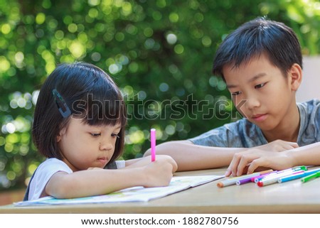 Cute Asian girls and boys, aged 4 to 10, sit outdoors in the garden, the brother is teaching her sister to write and draw with joy Smiling face Happily Is to enhance learning , The background is green