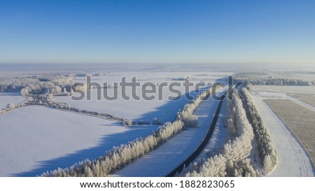 Winter road along the fields between cities aerial view from a drone. Winter landscape from a drone. Winter road view from a drone