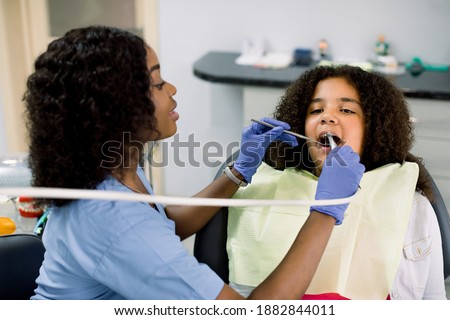 Close up view of little african american girl patient having dental treatment at dentist's office. Female black dentist making tooth caries treatment using drill and dental mirror Royalty-Free Stock Photo #1882844011