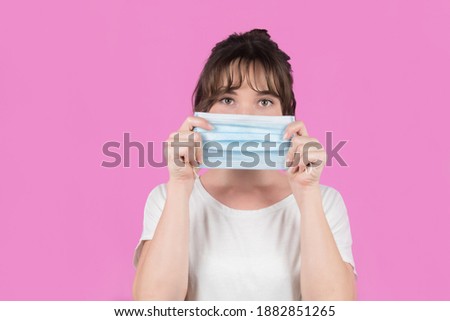 A young woman wears a mask to protect against COVID-19. Isolated on pink background. High quality photo