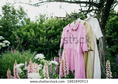 Natural colored dresses hanging on on a tree in the garden with lupine flowers. Concept organic clothes, eco-friendly, ecological fashion. Royalty-Free Stock Photo #1882890913
