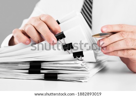 Businessman hands working in stacks of paper files for searching information on work desk home office, business concept.