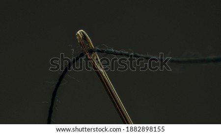 A black thread is passed through a gold needle.