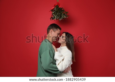 Happy couple standing under mistletoe bunch on red background