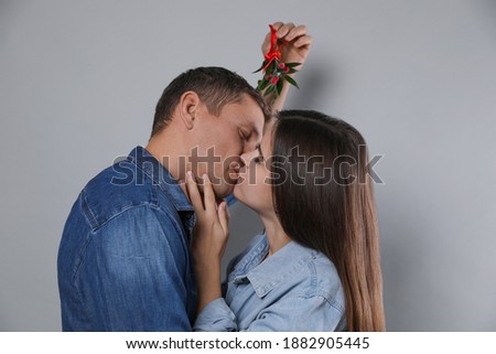 Happy couple kissing under mistletoe bunch on grey background