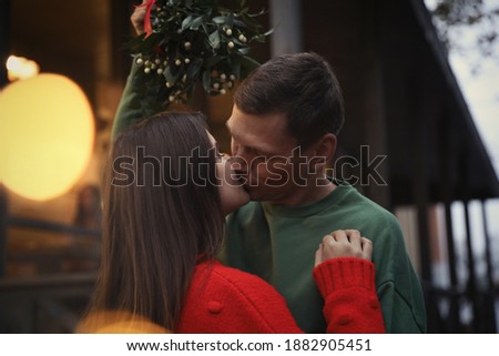 Happy couple kissing under mistletoe bunch outdoors