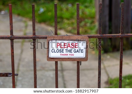 A please close the gate sign hanging on a rusty metal gate