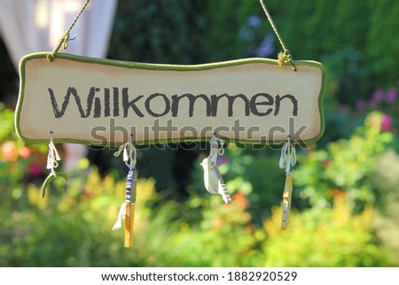 wooden sign in an garden - with "Willkommen" on it - the german word for welcome