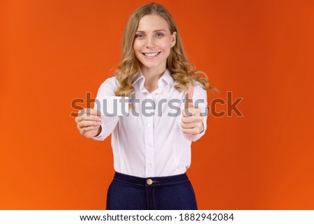 Cheerful young girl in white shirt holding empty business card and showing thumbs up isolated on red background