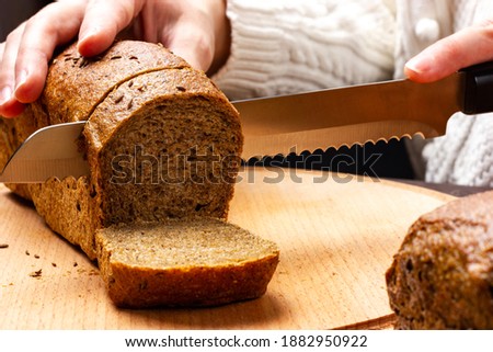 Women's hands, with a bread knife, cut fresh, crispy, rye bread. Slicing delicious bread. Royalty-Free Stock Photo #1882950922