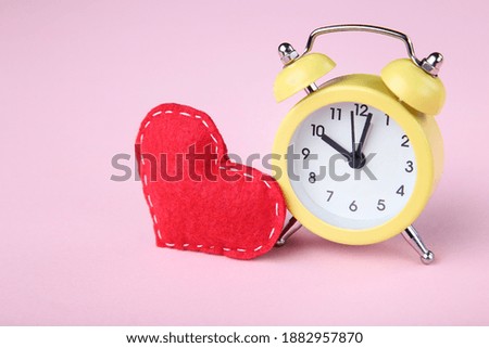 Yellow alarm clock with red fabric heart on pink background